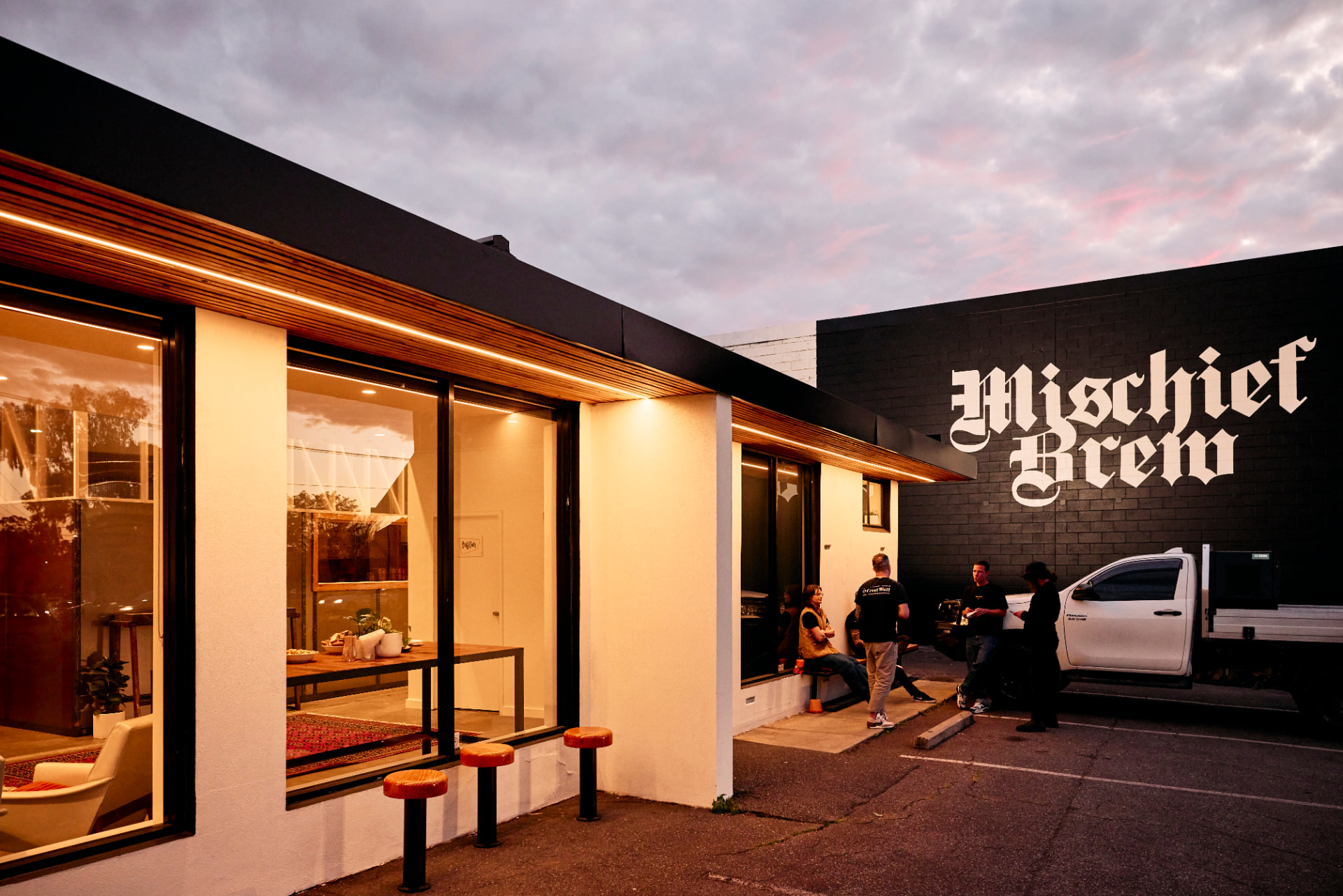 The Mischief Brew building in Norwood at dusk, with its name on the wall and people gathered out the front